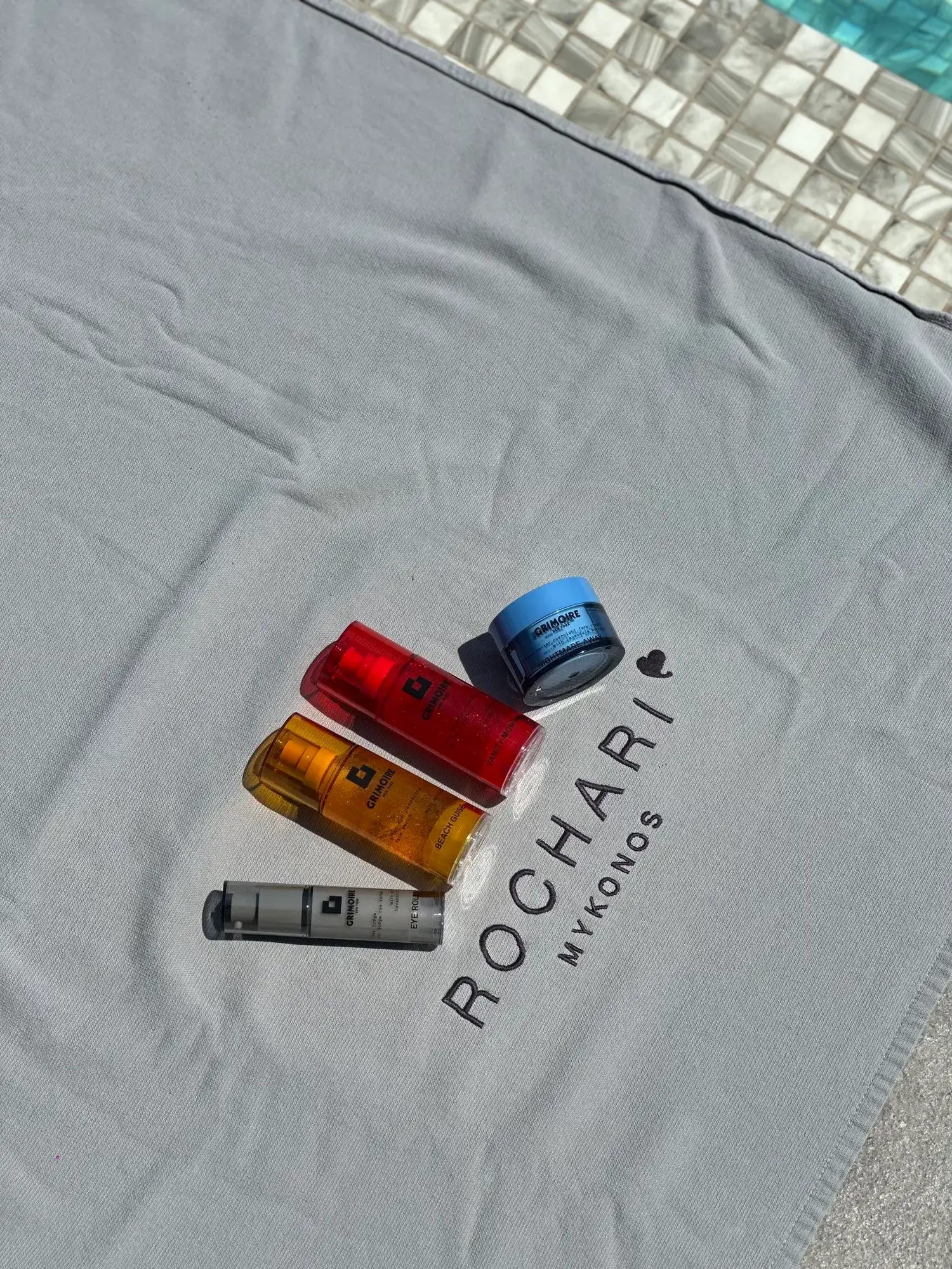 Grimoire NYC products displayed on a Rochari Hotel branded towel by the pool in Mykonos