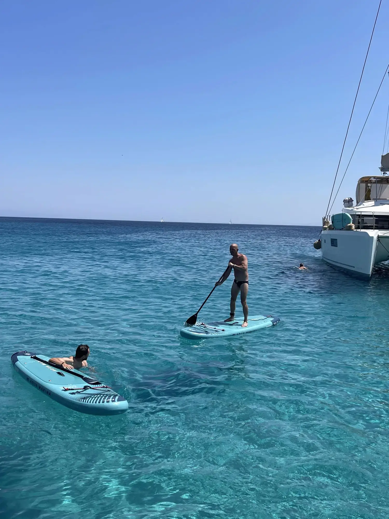 Guests paddleboarding in crystal-clear turquoise waters off the coast of Mykonos