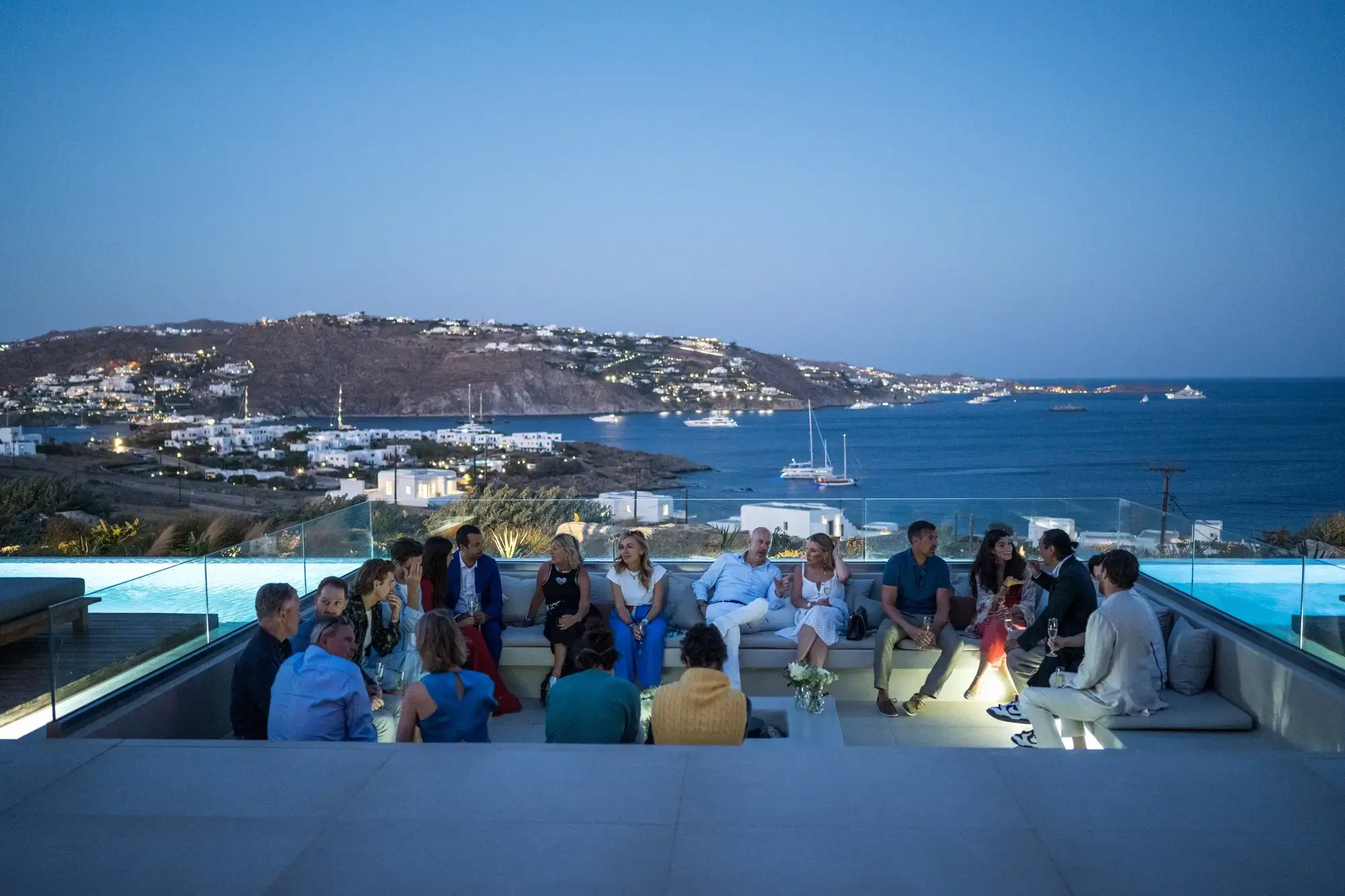 Blue hour at the villa: guests, conversation, and the lights of Mykonos Town